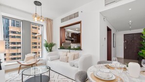 A modern living room with a glass coffee table, a sofa, and a dining area with a marble table set for four. - Gala Guests - 29 Boulevard Residences (Dubai)