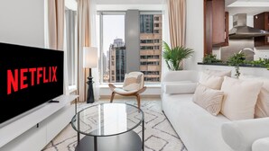 A modern living room with a large flat-screen TV, a glass coffee table, a sofa, and a view of a cityscape through large windows. - Gala Guests - 29 Boulevard Residences (Dubai)