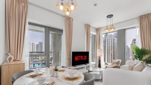 A modern living room with a dining area, a flat-screen TV, and large windows with a city view. - Gala Guests - 29 Boulevard Residences (Dubai)