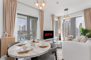 Ein modernes Wohnzimmer mit Essbereich, einem Flachbildfernseher und großen Fenstern mit Blick auf die Stadt.