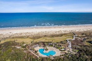 An aerial view of a resort with a swimming pool, beach access, and a clear view of the ocean.
