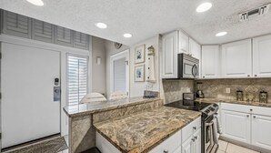 A kitchen with white cabinets, granite countertops, a microwave, stove, and a clock on the wall. - Oceanside with Pool, Hear the waves! Beach Walker Villas (Fernandina Beach)
