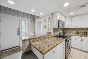 A kitchen with white cabinets, granite countertops, a microwave, stove, and a clock on the wall.