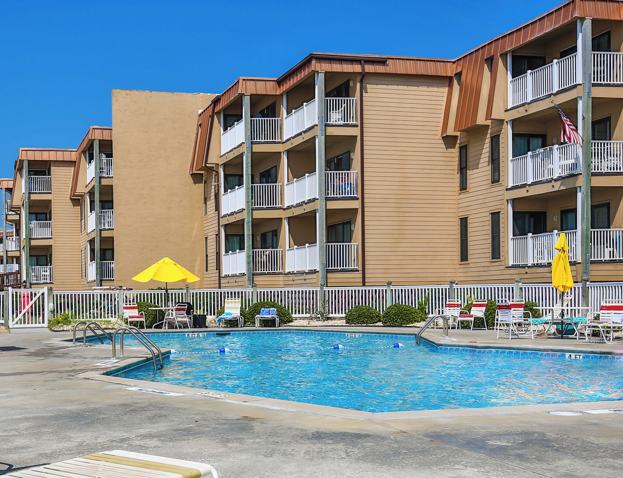 A hotel with a swimming pool, multiple balconies, and a yellow umbrella.