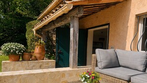 An outdoor seating area with a wicker sofa, a table with a woven top, and potted plants. - Charming Private Cottage with Garden & Parking in Bar-sur-Loup (Le Bar-sur-Loup)