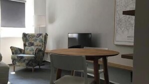 A dining area with a round table, two chairs, a patterned armchair, a television, and a pendant light. - A little dream in the heart of Innsbruck: Stylish apartment near the old town (Innsbruck)