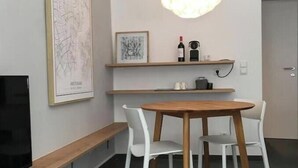 A dining area with a round wooden table, white chairs, a bench, a wall-mounted shelf with a wine bottle, and a framed abstract artwork. - A little dream in the heart of Innsbruck: Stylish apartment near the old town (Innsbruck)