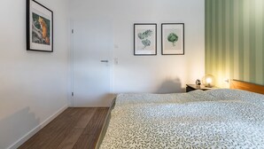 A bedroom with a bed, a door, two framed pictures, a nightstand with a lamp, and a green-striped wall. - Apartment "Hof Wuushöh" with Shared Garden, Balcony, and Wi-Fi (Stolk)
