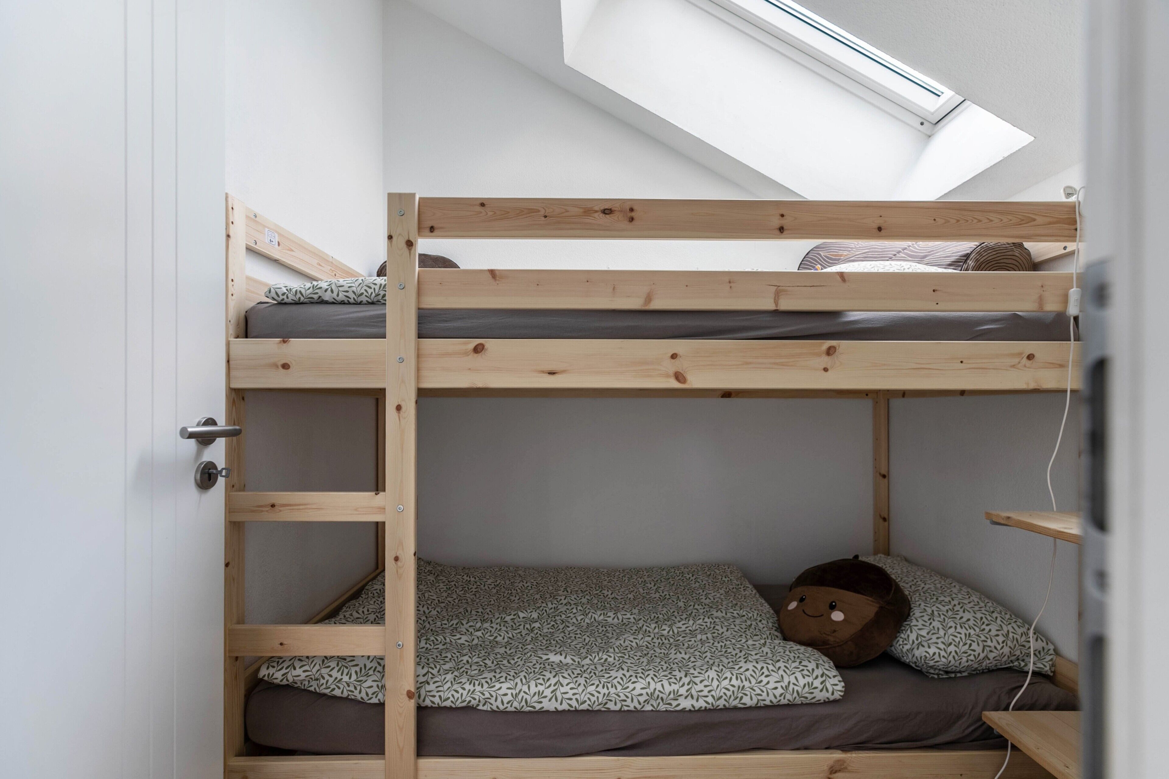 A bunk bed with a skylight above, a door on the left, and a shelf on the right.