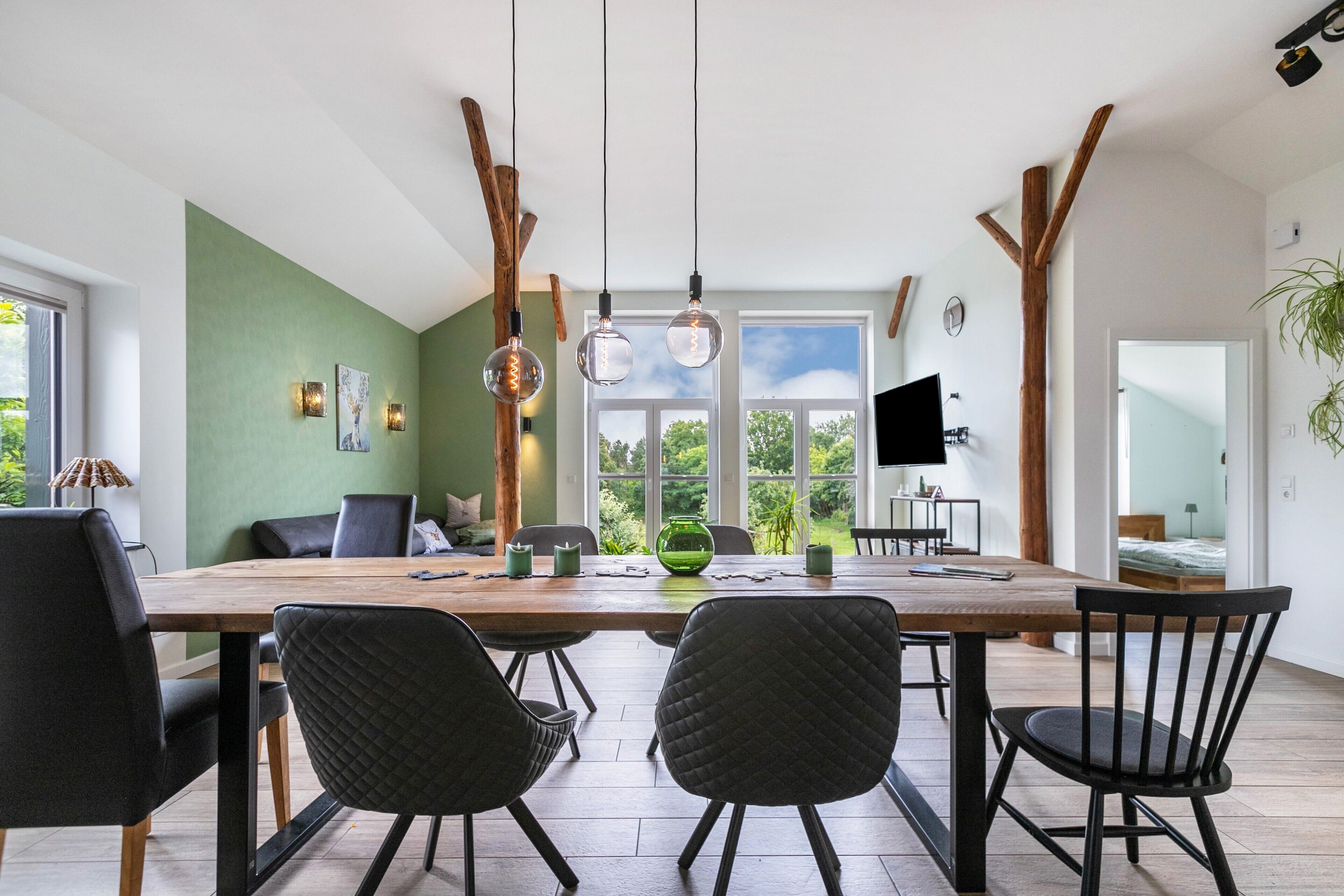 A dining area with a large wooden table, black chairs, and pendant lights.