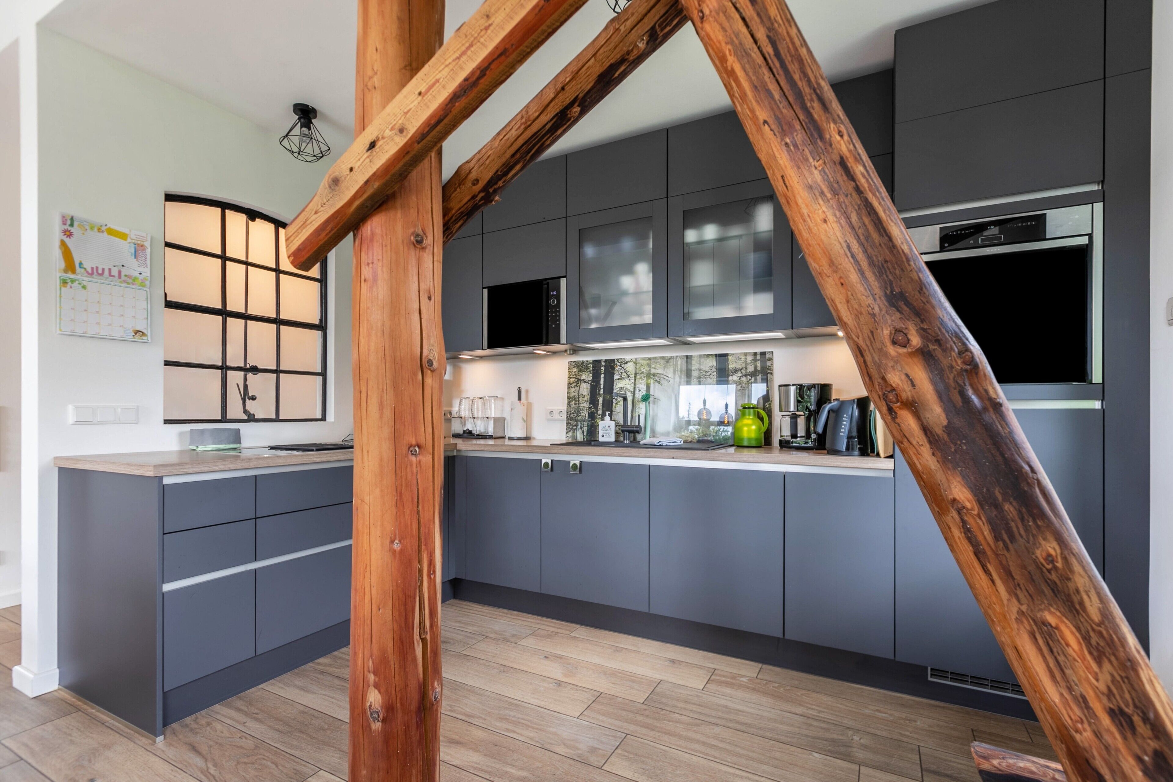 Eine moderne Küche mit grauen Schränken, sichtbarem Holzbalkenwerk und einer eingebauten Mikrowelle.