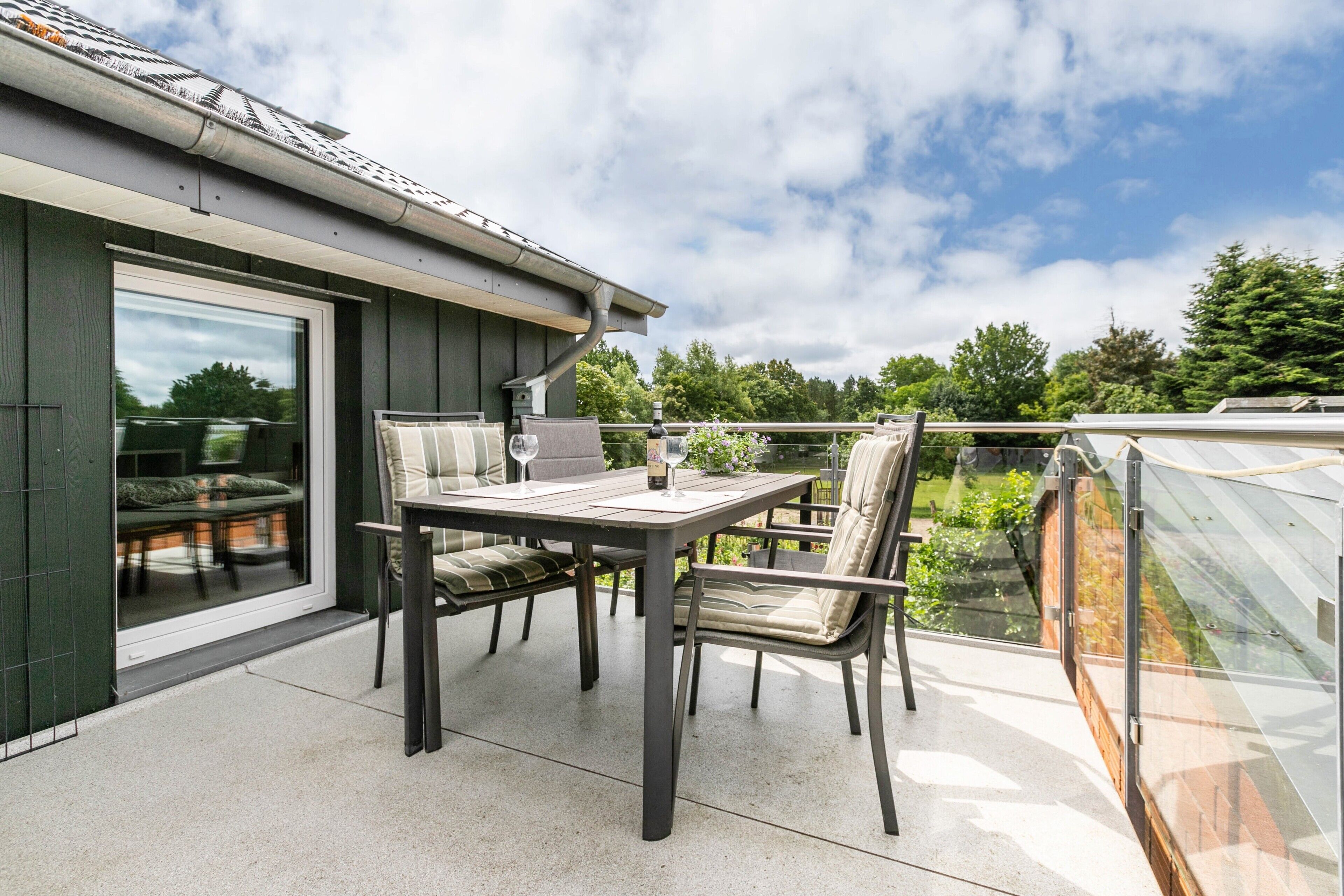 Eine Terrasse mit Tisch und Stühlen, eine Glastür, die zu einem Raum führt, und Blick ins Grüne.