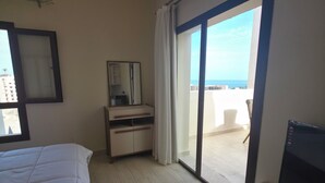 Ein Hotelzimmer mit Bett, Fernseher, Schreibtisch, Stuhl und Meerblick.