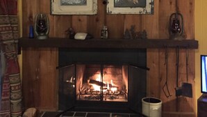 A wooden interior with a fireplace, two framed pictures, and a shelf with various items. - 3-bedroom cabin in charming Indian Lake (Indian Lake)