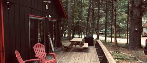 Une cabane avec une véranda, des chaises rouges et une table de pique-nique.