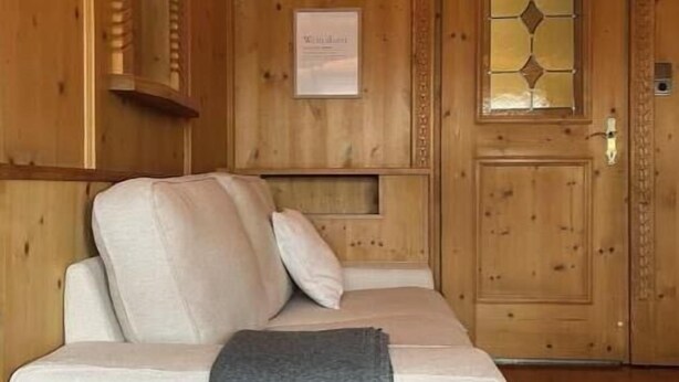 Una habitación con paneles de madera, un sofá, una puerta con un panel de vidrio y una lámpara fijada a la pared.
