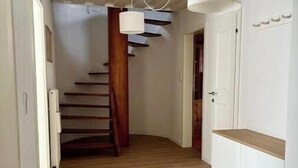 Un pasillo con suelo de madera, paredes blancas y una escalera de madera.