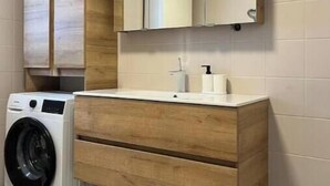 Un baño moderno con lavadora integrada, muebles de madera, un espejo y un lavabo con dispensador de jabón.
