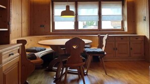 Un interior de madera con una mesa redonda, sillas y un ventanal con persianas.