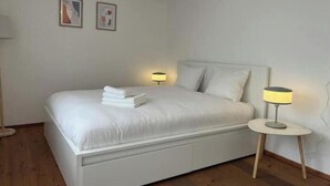 Una cama bien hecha con toallas dobladas, dos lámparas de noche y dos cuadros en la pared.