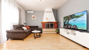 A living room with a sofa, a round coffee table, a fireplace, and a TV on the wall. - Villa Ariane with pool (Policnik)