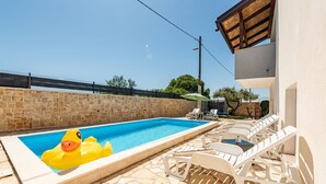 A swimming pool with inflatable ducks, lounge chairs, and a stone wall. - Villa Ariane with pool (Policnik)