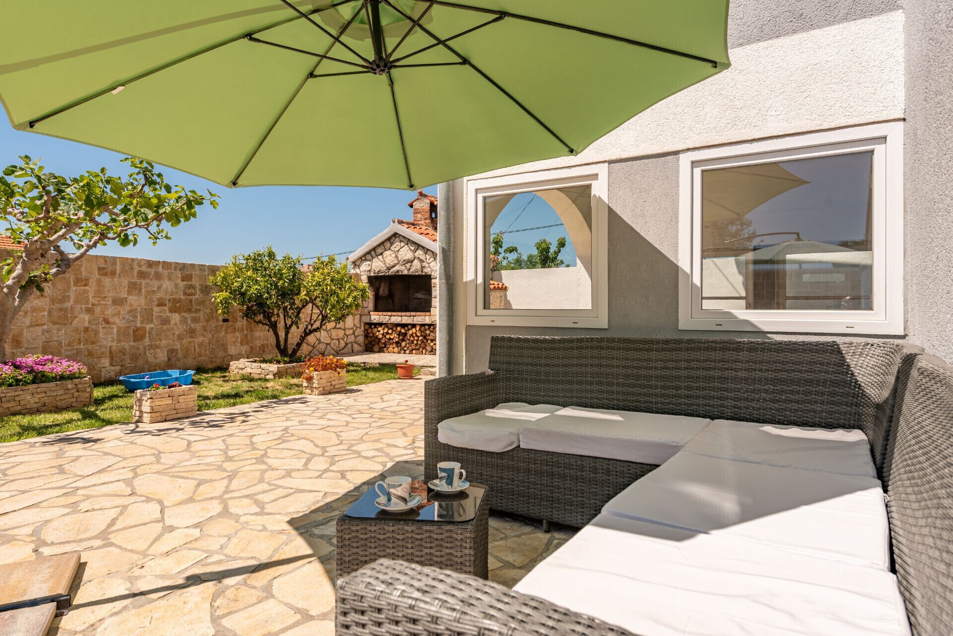 A patio with a wicker sofa, a table with a cup, and a green umbrella.