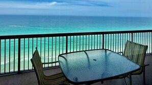 Un balcon avec une table et des chaises en verre, donnant sur une mer turquoise et un ciel dégagé.