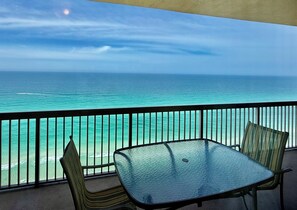 A balcony with a glass table and chairs, overlooking a turquoise sea and clear sky. - Master on Gulf & close to Everything & Free round of Golf & Activities Daily! (Panama City Beach)