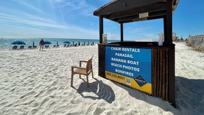 Un petit kiosque situé sur la plage, avec une enseigne indiquant la location de chaises longues, les activités de parachute ascensionnel, les promenades en bouée tractée, les séances de photos sur la plage et les feux de joie.
