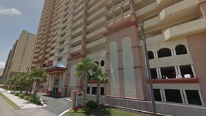 Un hôtel à plusieurs étages doté de balcons, une enseigne indiquant « Sunrise Beach Condominium », et un parking bordé de palmiers.