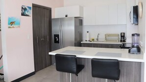 A modern kitchen with a refrigerator, a coffee maker, a blender, and two bar stools. - Great apartment near the Airport with Air Condit. (Alajuela)