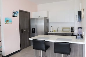 Una cocina moderna con refrigerador, cafetera, licuadora y dos taburetes de bar.