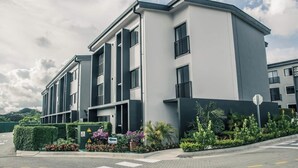 A modern multi-story residential building with balconies, a landscaped garden, and a clear sky. - Great apartment near the Airport with Air Condit. (Alajuela)