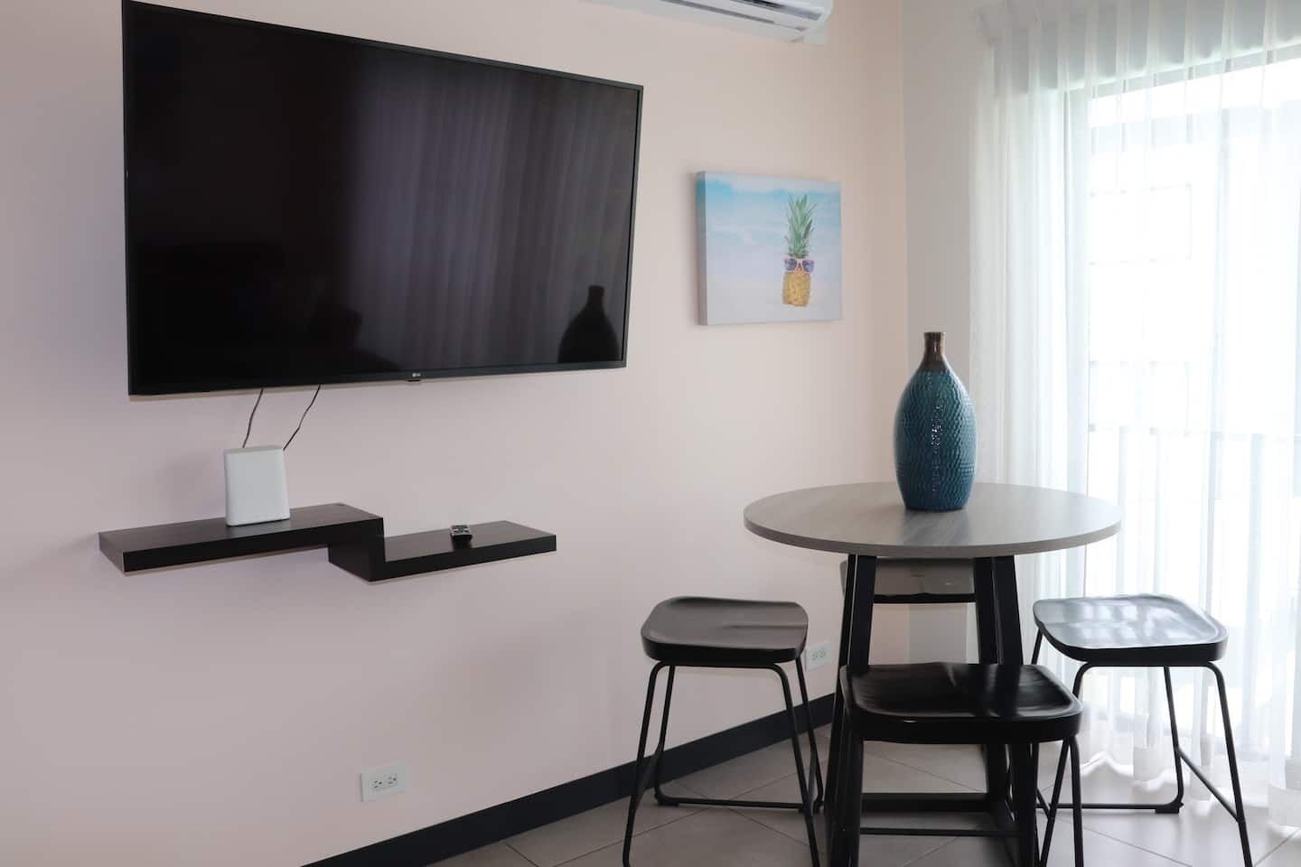 A modern room with a flat-screen TV, a small table with chairs, and a painting on the wall.