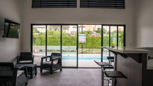 A modern indoor pool area with a view of a residential neighborhood, including a sign for 'HOMETOWN'. - Great apartment near the Airport with Air Condit. (Alajuela)