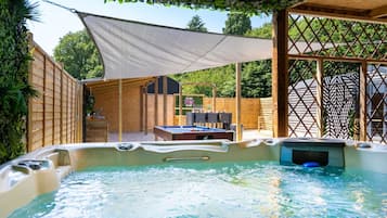 A hot tub with a wooden deck and a table with chairs in the background.