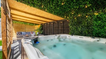 A hot tub with a wooden deck and a green wall.