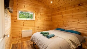 A wooden cabin room with a bed, a window, and a heater. - The Cabin  @The Outside Inn (Mountfield)