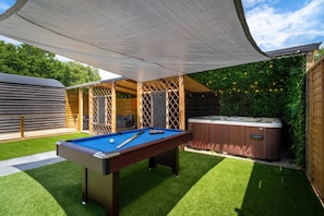 A pool table with a hot tub and a covered seating area in a backyard.