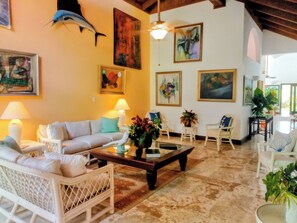 Ein geräumiges Wohnzimmer mit hohen Decken, weißen Möbeln und unterschiedlichen Wandbildern.