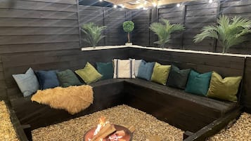 Un espace salon accueillant avec un foyer, entouré d’un banc de couleur sombre agrémenté de coussins.