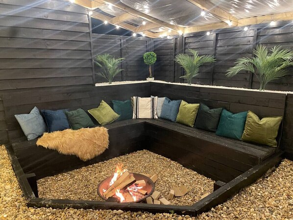 A cozy seating area with a fire pit, surrounded by a dark-colored bench with cushions.