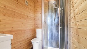 Un baño de cabaña de madera con ducha de vidrio, un inodoro blanco y un lavamanos blanco.