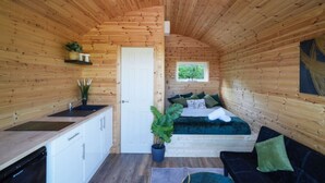 Una cabaña de madera compacta con kitchenette, una cama con ropa de cama verde y un ventanal pequeño.
