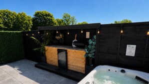 Un jacuzzi con muelle de madera y un letrero, rodeado por un seto y una cerca de madera.