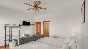 Une chambre avec un lit, un ventilateur de plafond, un téléviseur fixé au mur et une porte sur laquelle est apposée une pancarte indiquant « FERMÉ ».