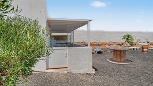 Une cuisine extérieure moderne avec vue sur la plage, un espace salon couvert et une petite table avec des chaises.