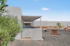 Een moderne buitenkeuken met uitzicht op het strand, een overdekte zithoek en een kleine tafel met stoelen.