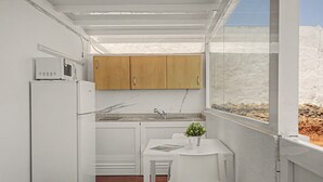 Une cuisine compacte avec des meubles blancs, un four à micro-ondes encastré et un petit coin repas comprenant une table et une chaise.